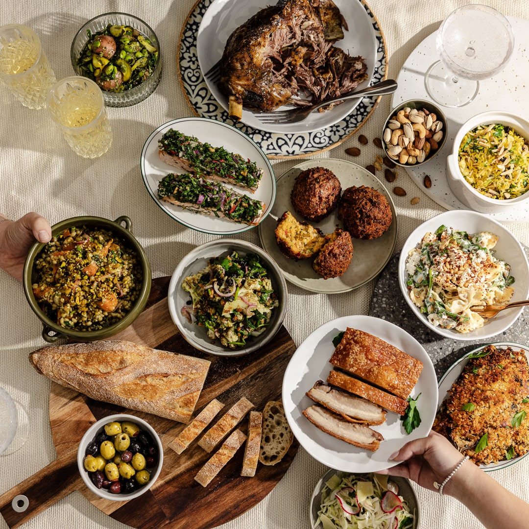 Overhead view of a diverse meal spread with roasted meats, grain salads, falafel, and fresh bread